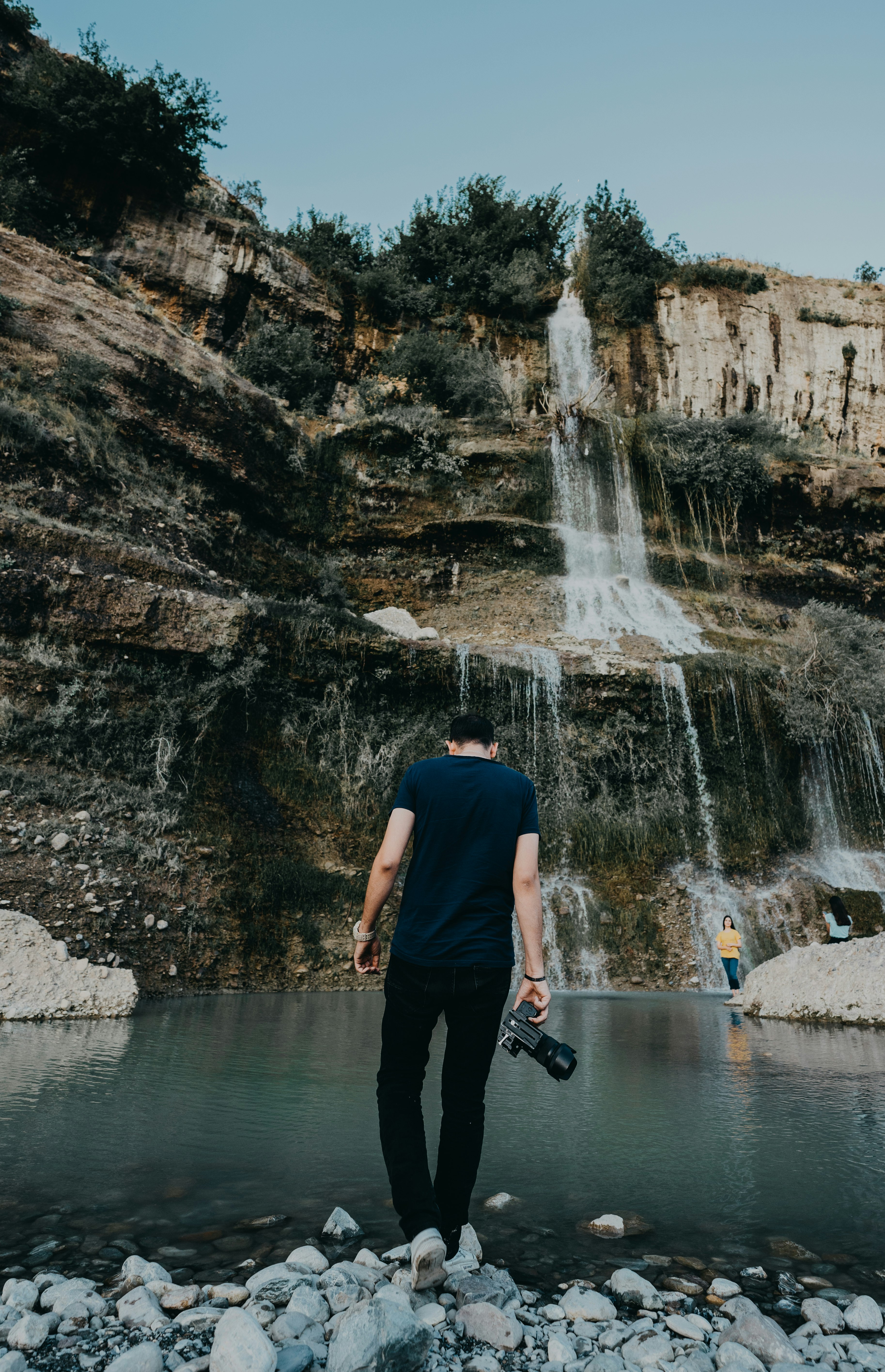 man in black t-shirt and black pants standing in front of waterfalls during daytime